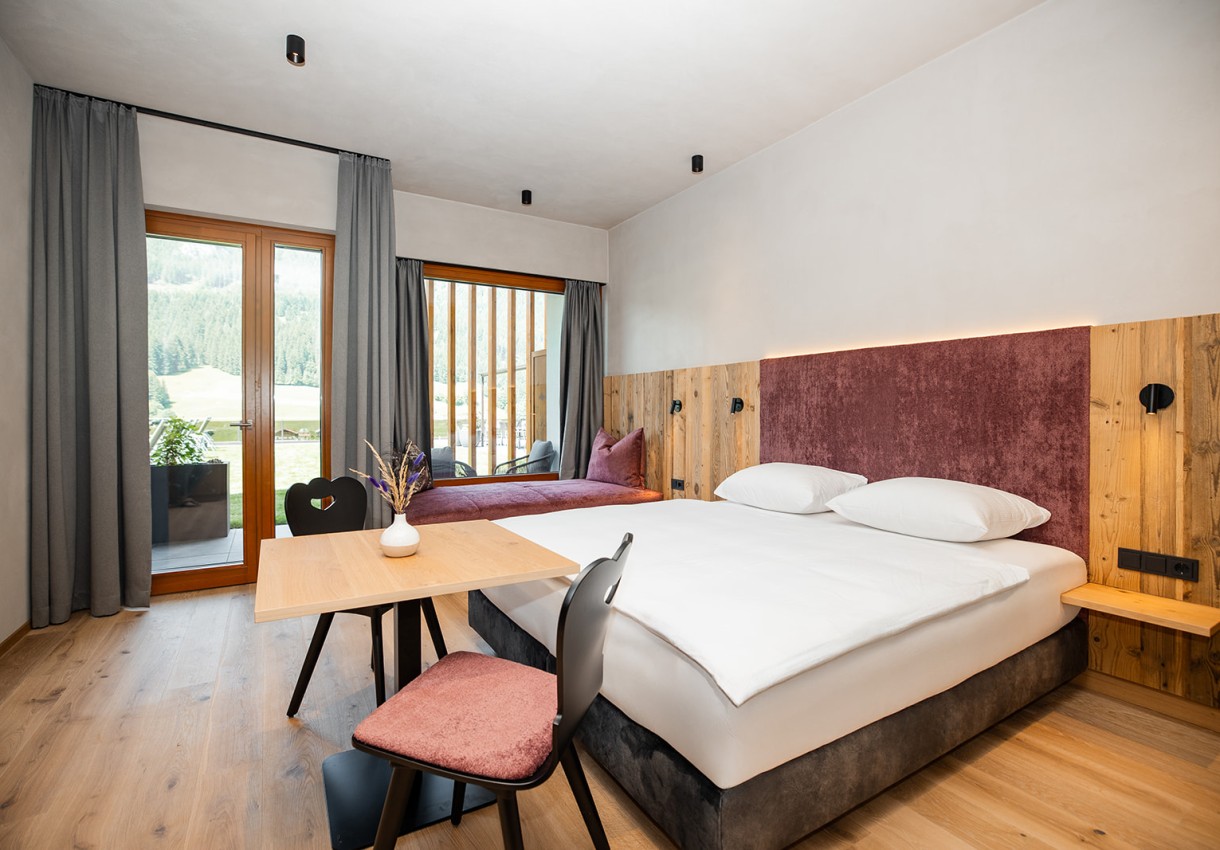 Stilvolle Suite mit Doppelbett, warmen Holzelementen und Ausblick ins Grüne im Hotel Dorfer